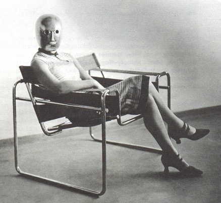 Charlotte Perriand, portant un masque de théâtre au Bauhaus, pose assise dans un des fauteuils à structure metallique, conçu par Marcel Breuer. JPEG - 75.4 ko