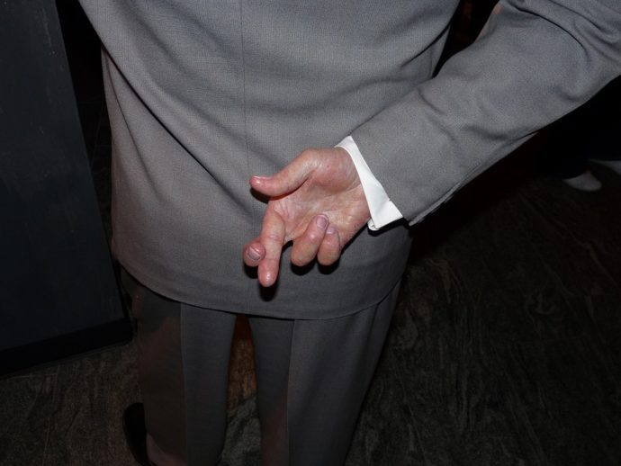 personnage en costume gris, les doigts de la main droite croisés dans le dos