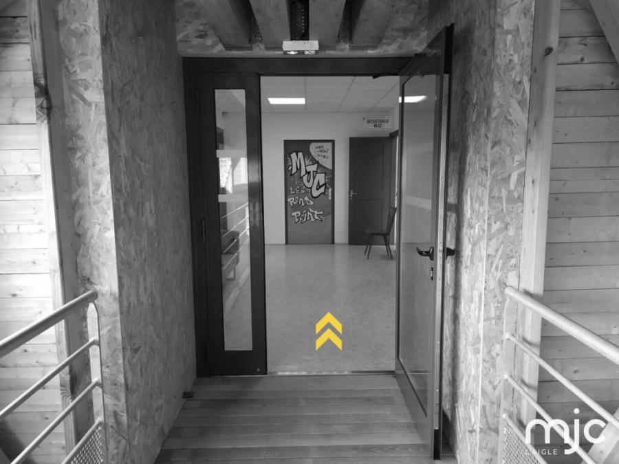 photo noir/blanc de l'entrée de la MJC, chevrons jaunes pointe vers le haut pour indiquer le sens de l'entrée. on distingue le graph sur une porte : MJC Le rond-point